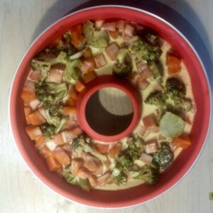 A red silicone mold shaped like a doughnut with vegetables in it.