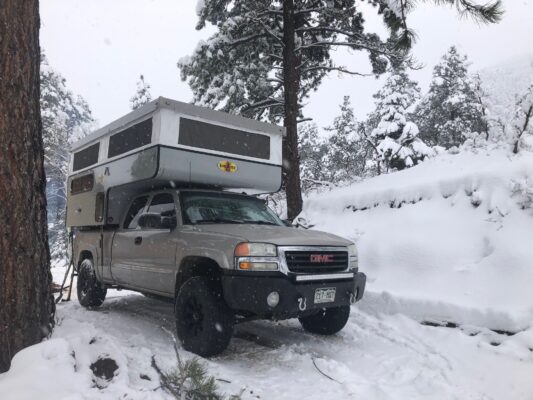 A truck parked in the snow with a camper on top.