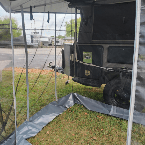 A black truck parked under a tarp on the grass.