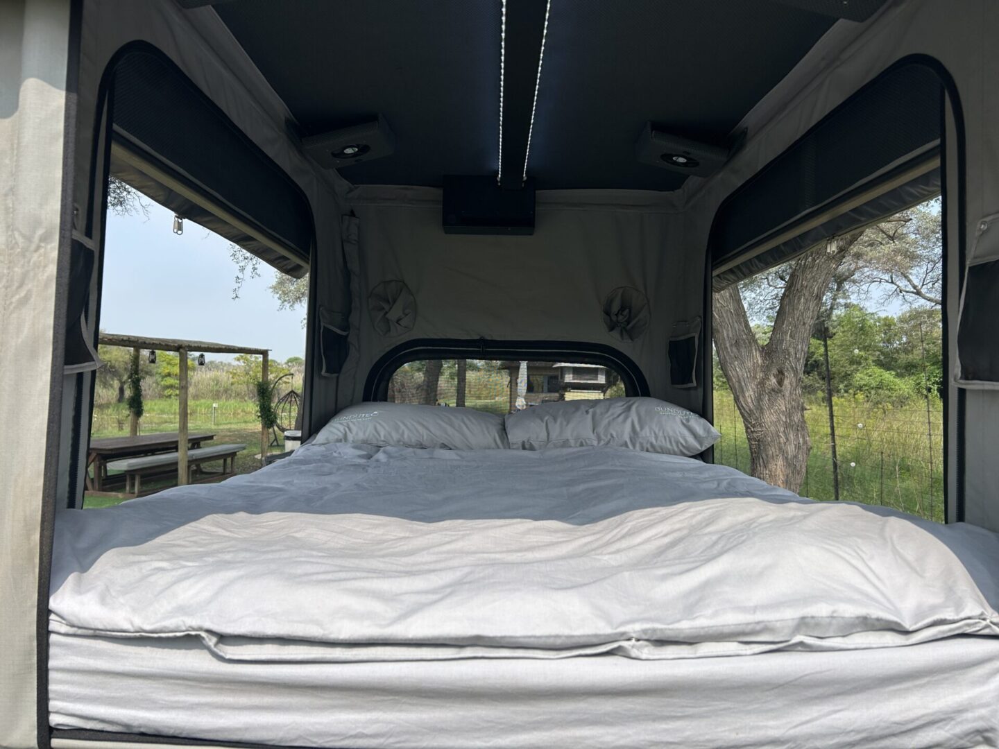 Cozy bed inside open camper with view.