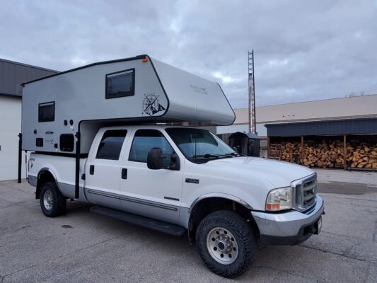 White truck with camper parked outside building.