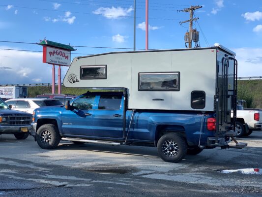 Blue truck with large camper parked outside.